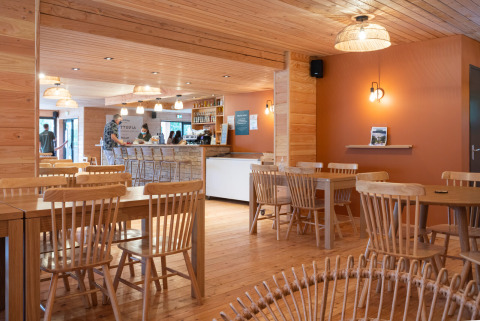 Intérieur de café en bois avec tables et chaises à Huttopia Pays de Cordes sur Ciel en Occitanie, France.