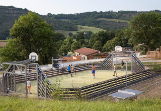 Børn spiller boldspil på en udendørs bane omgivet af træer i ferieparken Huttopia Pays de Cordes sur Ciel.