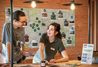 Receptionist hjælper en gæst med kort og turistinformation på ferieparken Huttopia Pays de Cordes sur Ciel.