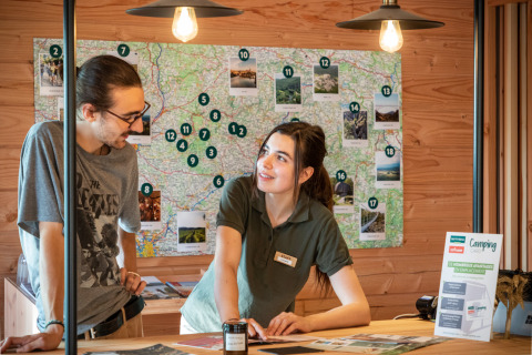 Receptionist assiste un ospite con mappe al parco vacanze Huttopia Pays de Cordes sur Ciel in Occitania, Francia.