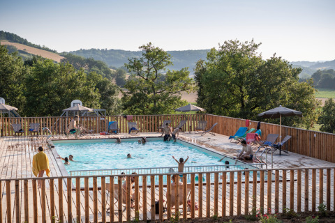Huéspedes disfrutan de la piscina con vistas a las colinas en Huttopia Pays de Cordes sur Ciel, Occitania, Francia.