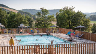 Huéspedes disfrutan de la piscina con vistas a las colinas en Huttopia Pays de Cordes sur Ciel, Occitania, Francia.