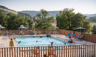 Huéspedes disfrutan de la piscina con vistas a las colinas en Huttopia Pays de Cordes sur Ciel, Occitania, Francia.
