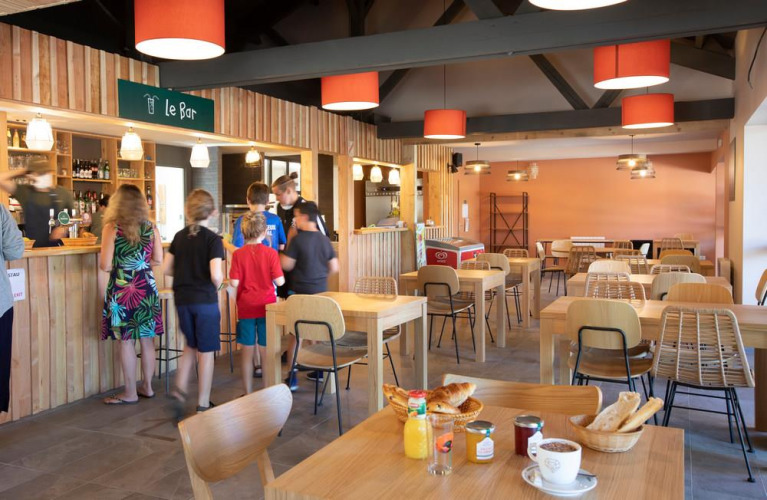 Binnen café bij Huttopia Pays de Cordes sur Ciel, Occitanië, Frankrijk, met gasten aan de houten bar.