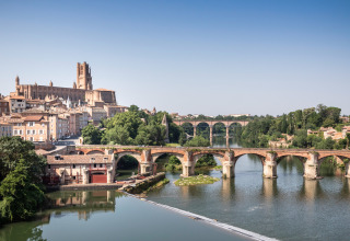 View of a historic stone bridge and the Albi Cathedral beside a river near Vindrac Alayrac, Occitanie, France.