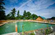 Naturlig swimmingpool med solsenge og træhytte ved Village Huttopia Senonches i Centre-Val de Loire, Frankrig.