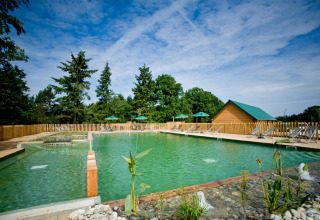 Naturpool mit Liegestühlen und Holzhütte im Village Huttopia Senonches, Centre-Val de Loire, Frankreich.