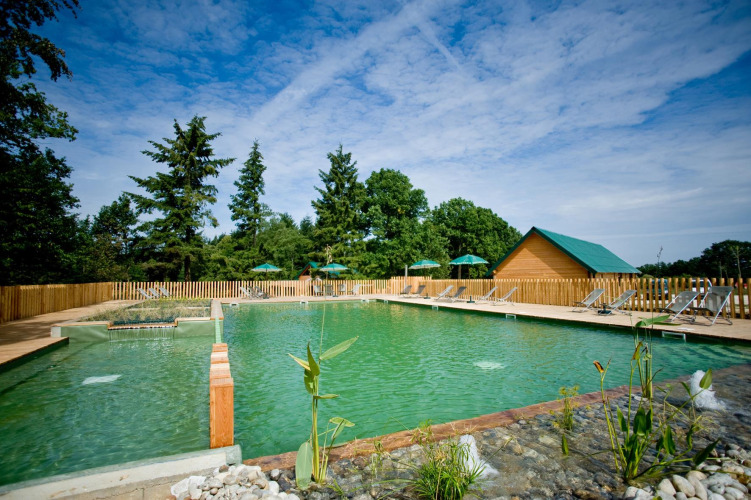 Natural swimming pool with sun loungers and a wooden hut at Village Huttopia Senonches, Centre-Val de Loire, France.