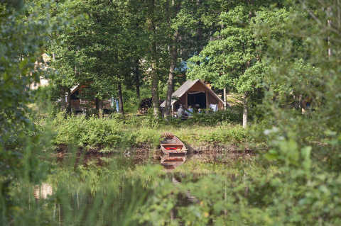 Tienda de campaña junto a un lago rodeada de frondosos árboles en el parque vacacional Huttopia Senonches.