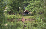 A tent by the lakeside surrounded by lush woods and a small boat in Huttopia Senonches holiday park.