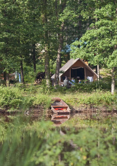 Tienda de campaña junto a un lago rodeada de frondosos árboles en el parque vacacional Huttopia Senonches.