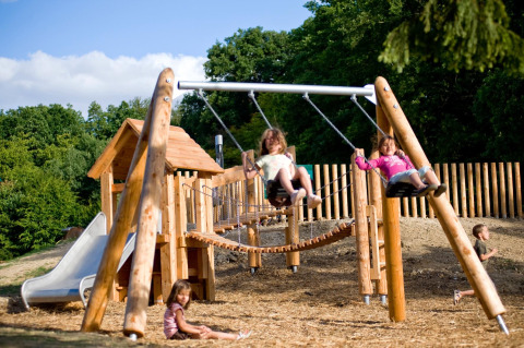 Kinder spielen auf einem Spielplatz mit Schaukeln und Rutsche im Village Huttopia Senonches, Frankreich.