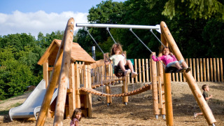 Niños juegan en un parque infantil con columpios y tobogán en Village Huttopia Senonches, Francia.