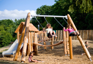 Niños juegan en un parque infantil con columpios y tobogán en Village Huttopia Senonches, Francia.