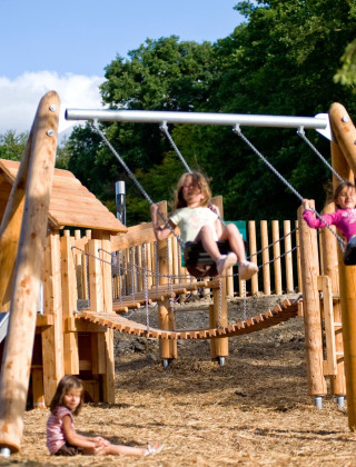 Niños juegan en un parque infantil con columpios y tobogán en Village Huttopia Senonches, Francia.