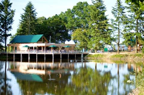 Edificio de madera junto al lago con sombrillas verdes y árboles alrededor en Village Huttopia Senonches.