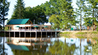Edificio de madera junto al lago con sombrillas verdes y árboles alrededor en Village Huttopia Senonches.
