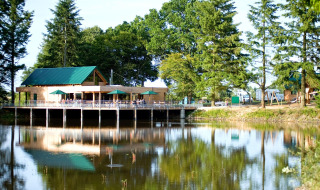 Edificio de madera junto al lago con sombrillas verdes y árboles alrededor en Village Huttopia Senonches.