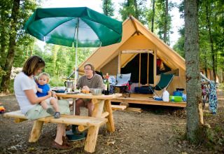 Family enjoying outdoor meal at picnic table with large tent in the forest at Village Huttopia Senonches, France.