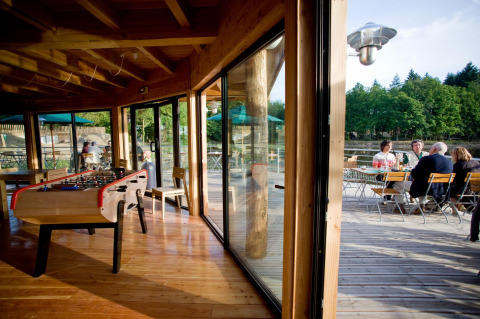 Mesa de futbolín interior y terraza exterior con huéspedes en Village Huttopia Senonches, Francia