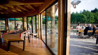 Mesa de futbolín interior y terraza exterior con huéspedes en Village Huttopia Senonches, Francia