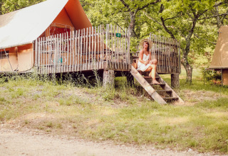 Vrouw op de trap van een lodge-tent in Village Huttopia Dieulefit, omringd door bomen in Frankrijk.