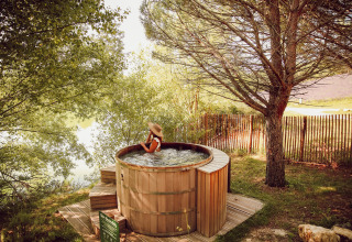 Vrouw die geniet in een houten hottub buiten, omringd door natuur in Village Huttopia Dieulefit, Frankrijk.
