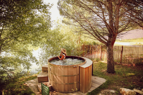 Woman relaxing in an outdoor wooden hot tub surrounded by trees at Village Huttopia Dieulefit, France.