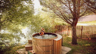 Mujer relajándose en una bañera de hidromasaje de madera al aire libre en Village Huttopia Dieulefit, Francia.