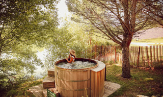 Mujer relajándose en una bañera de hidromasaje de madera al aire libre en Village Huttopia Dieulefit, Francia.