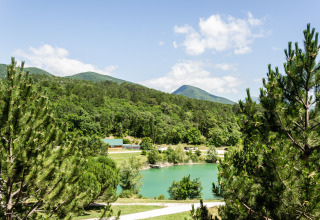 Panoramablick auf einen grünen Ferienpark mit See und bewaldeten Bergen in Auvergne-Rhône-Alpes, Frankreich.