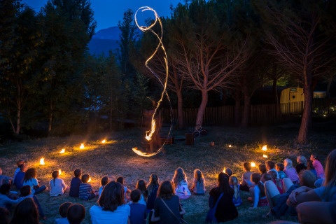 Kinder schauen eine Feuershow in einem Kreis im Freien im Feriendorf Huttopia Dieulefit in Frankreich an.