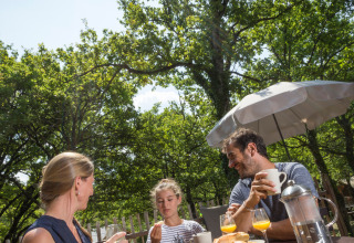 Family having outdoor breakfast in the sun surrounded by greenery at Village Huttopia Dieulefit, France.