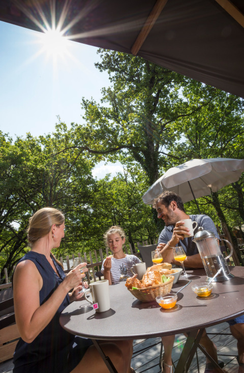 Family having outdoor breakfast in the sun surrounded by greenery at Village Huttopia Dieulefit, France.