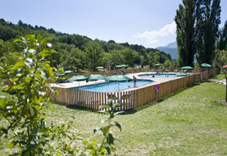 Swimmingpool i ferieparken Huttopia Dieulefit, omgivet af grønne træer og bjerge i Auvergne-Rhône-Alpes.