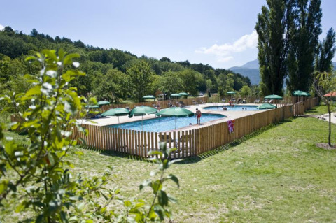 Swimmingpool i ferieparken Huttopia Dieulefit, omgivet af grønne træer og bjerge i Auvergne-Rhône-Alpes.