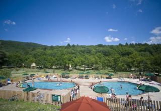 Solrige gæster nyder to swimmingpools omgivet af grønne træer i Village Huttopia Dieulefit, Frankrig.