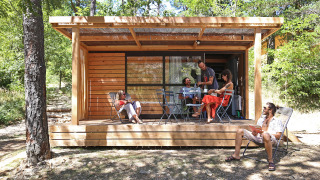Fünf Menschen entspannen sich auf der Terrasse der Chalet Evasion Hütte, umgeben von Wald.