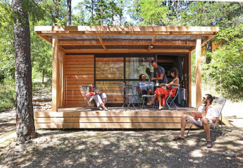 Fünf Menschen entspannen sich auf der Terrasse der Chalet Evasion Hütte, umgeben von Wald.
