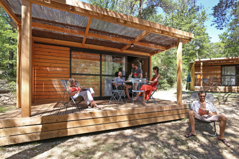 Fem personer slapper af på verandaen ved en træhytte på Camping d'Angers - Lac de Maine, solrig dag.