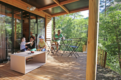 Famiglia che si rilassa sulla veranda in legno dello Chalet Evasion al Camping d'Angers - Lac de Maine in Francia.