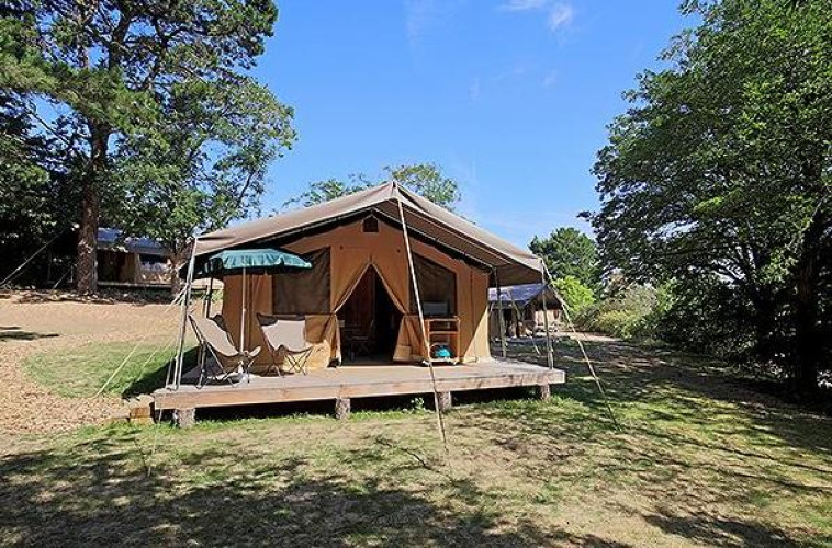 Tienda safari Tent Sweet con terraza, sillas y sombrilla, rodeada de naturaleza bajo un cielo azul claro.