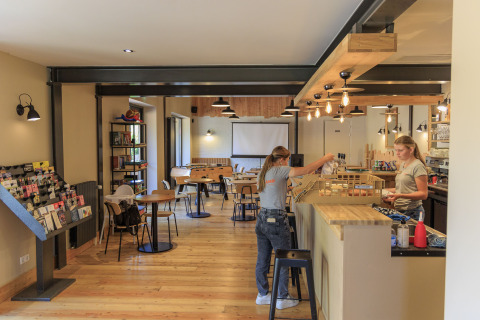 Zona de cafetería moderna en Camping Valkenburg - Maastricht, Limburg, con personal y áreas de mesas.
