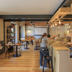 Zona de cafetería moderna en Camping Valkenburg - Maastricht, Limburg, con personal y áreas de mesas.