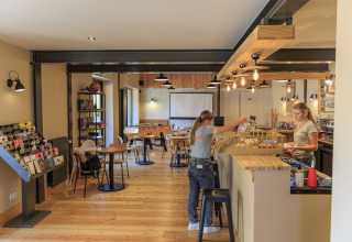 Moderne caféområde på Camping Valkenburg - Maastricht, Limburg, med personale bag disken og borde.