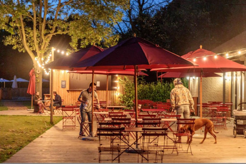 Outdoor dining area at Camping Valkenburg - Maastricht in Limburg, Netherlands, with guests and a dog.