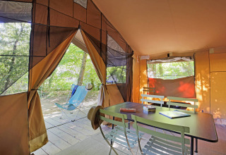 Interno di una tenda Sweet Toile&Bois con tavolo, sedie e vista sulla natura dall’ingresso aperto.