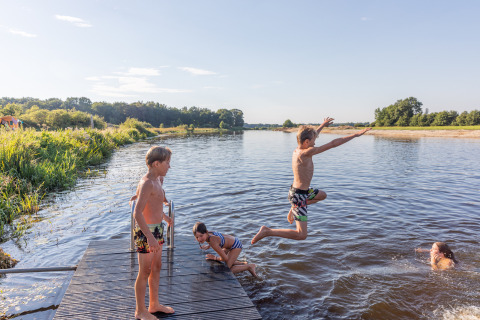 Niños saltan al agua desde un muelle de madera en Huttopia De Roos, parque vacacional en Overijssel, Países Bajos.