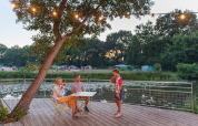 Familie nyder aftenen ved et bord på en terrasse med udsigt til sø og telte på Huttopia De Roos, Overijssel.