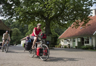 Cykelturister nyder en tur ved Huttopia De Roos feriepark i Overijssel, Holland, omgivet af natur og hytter.